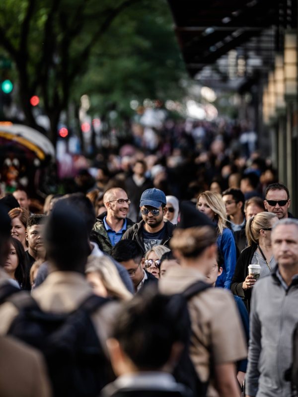 A bustling urban scene with diverse people walking on a tree-lined city street.