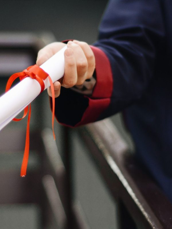 A close-up image of a graduate holding a diploma tied with a red ribbon, symbolizing achievement and success.